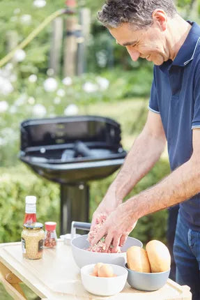 Zwarte houtskoolbarbecue met geopend deksel; hand bereidt eten op het rooster