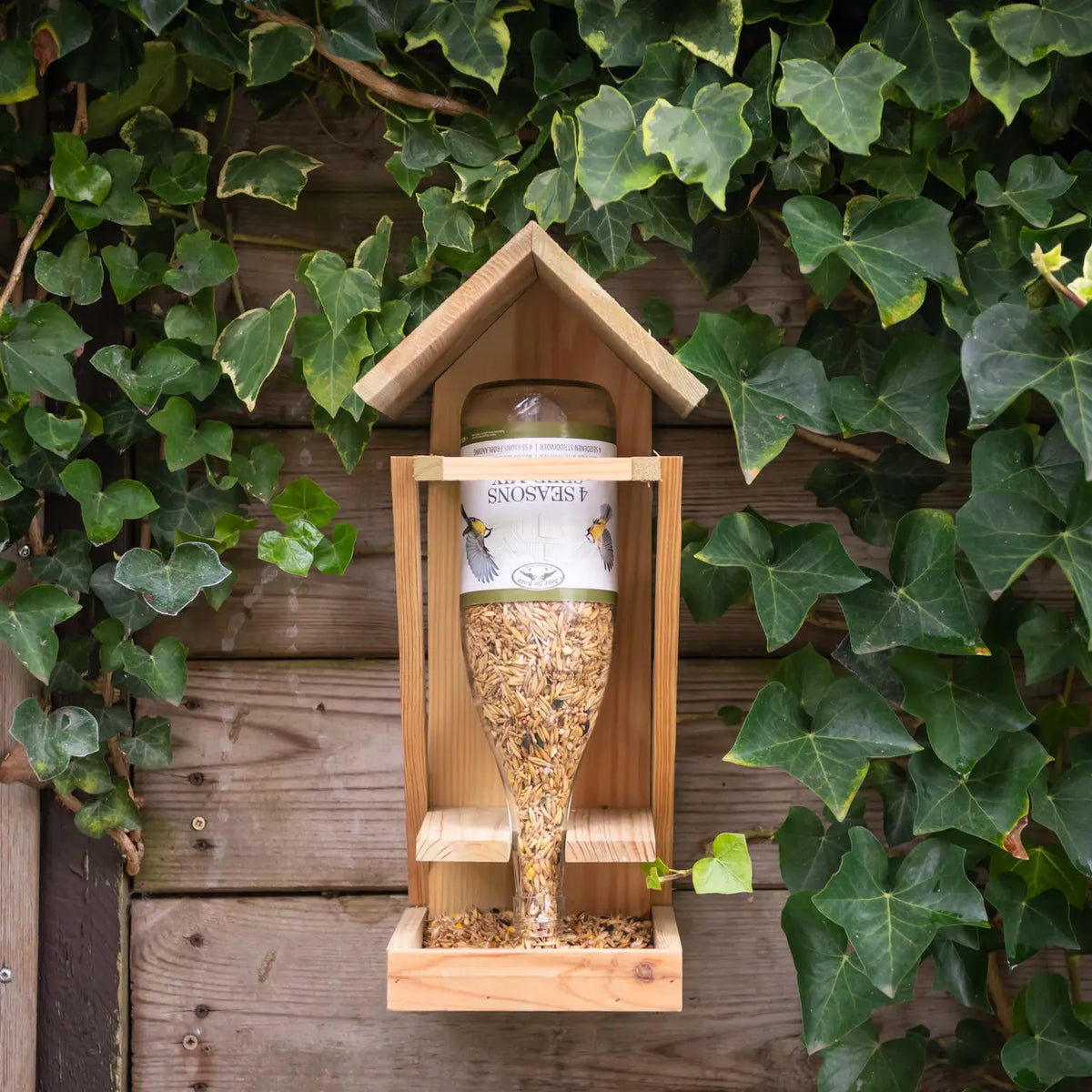 Houten wijnflesvoedertafel met glazen fles vol vogelzaad, houten dakje