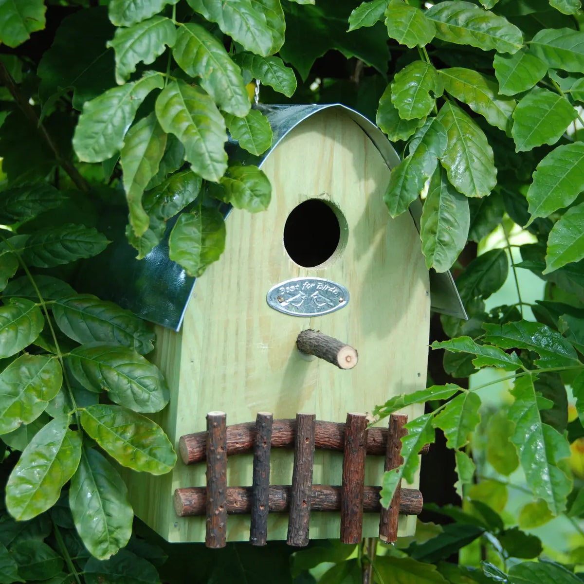 Landelijke houten nestkastje met ronde ingang, metalen plaat en houten spijlen, licht van kleur.