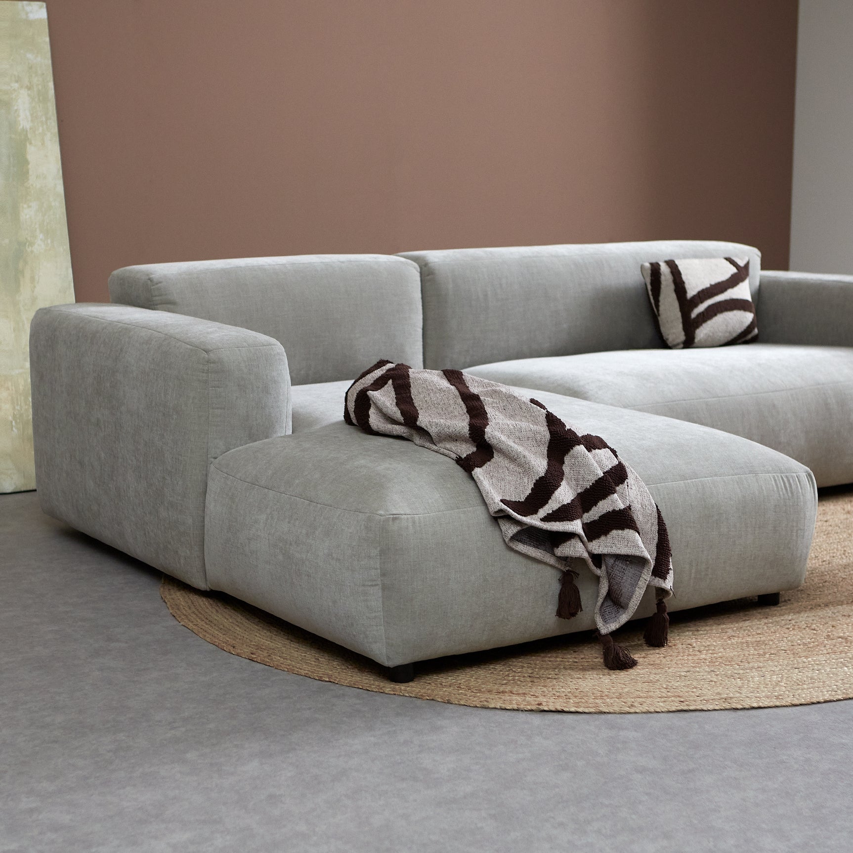 Grijze chaise longue met opstaande armleuning en sierkussens, plaid over de zitting