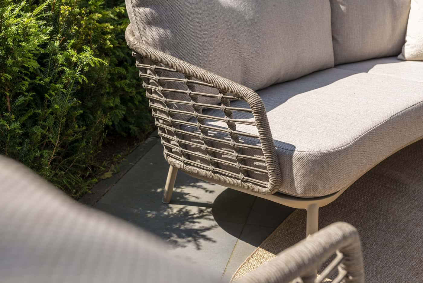 Beige lounge stoel met gevlochten zijkant en beige kussens op terras