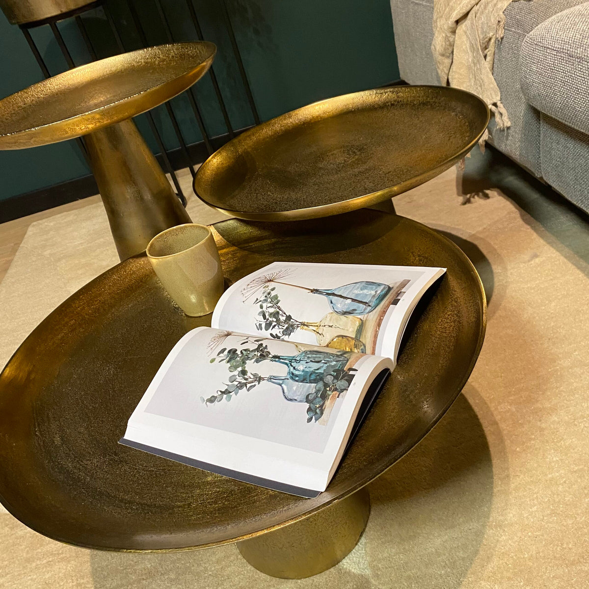 Gouden ronde salontafel met twee bladen, mok en open magazine op het oppervlak