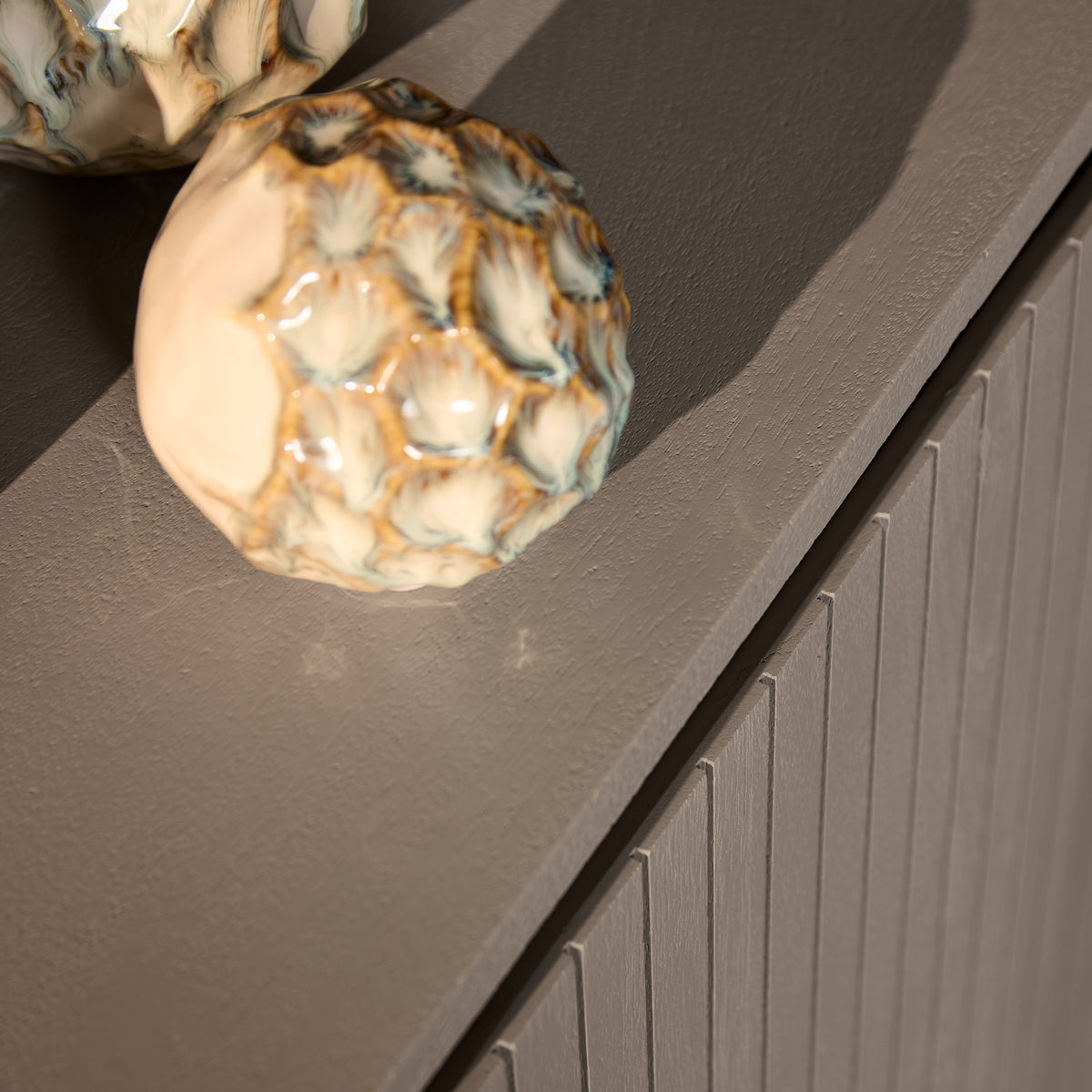 Dressoir hoekdetail: afgeronde bovenkant en geribbelde deurenfront, grijs-taupe.