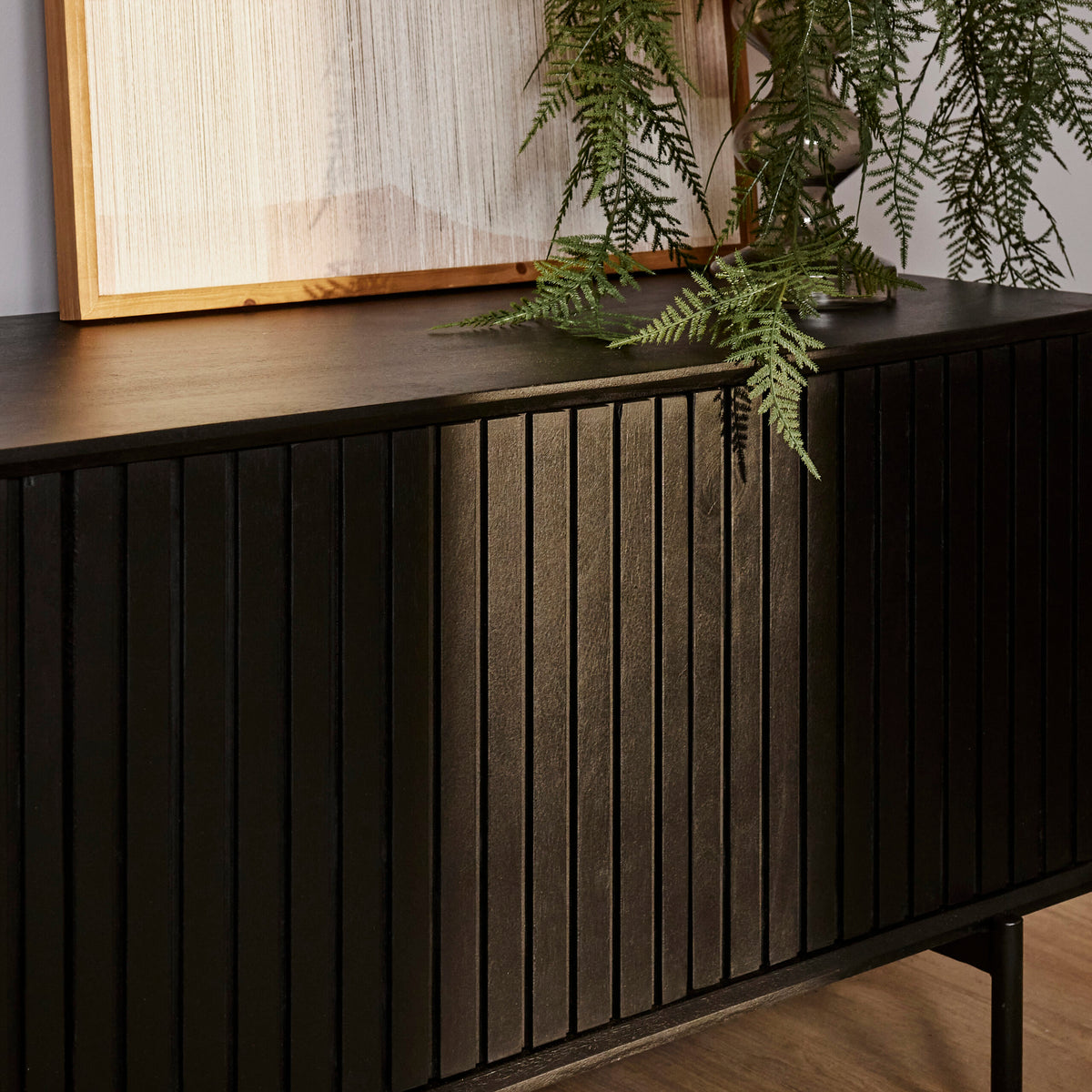 Zwart tv-meubel front met verticale ribbels en deurpanelen, lage kast op poten.