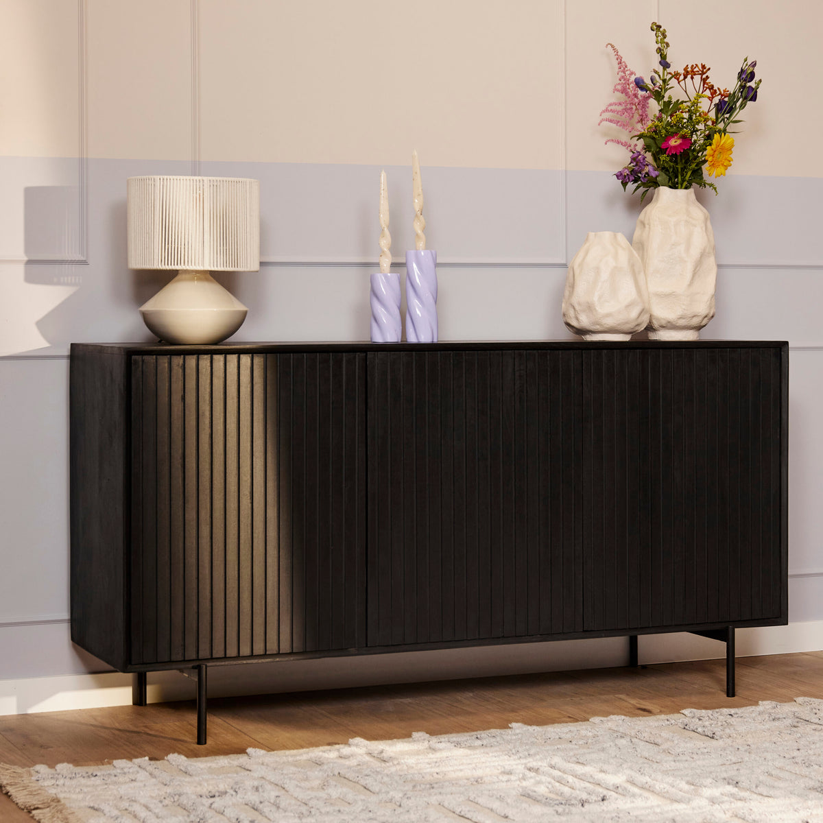 Zwart dressoir met deuren en verticale ribbels, op smalle poten.