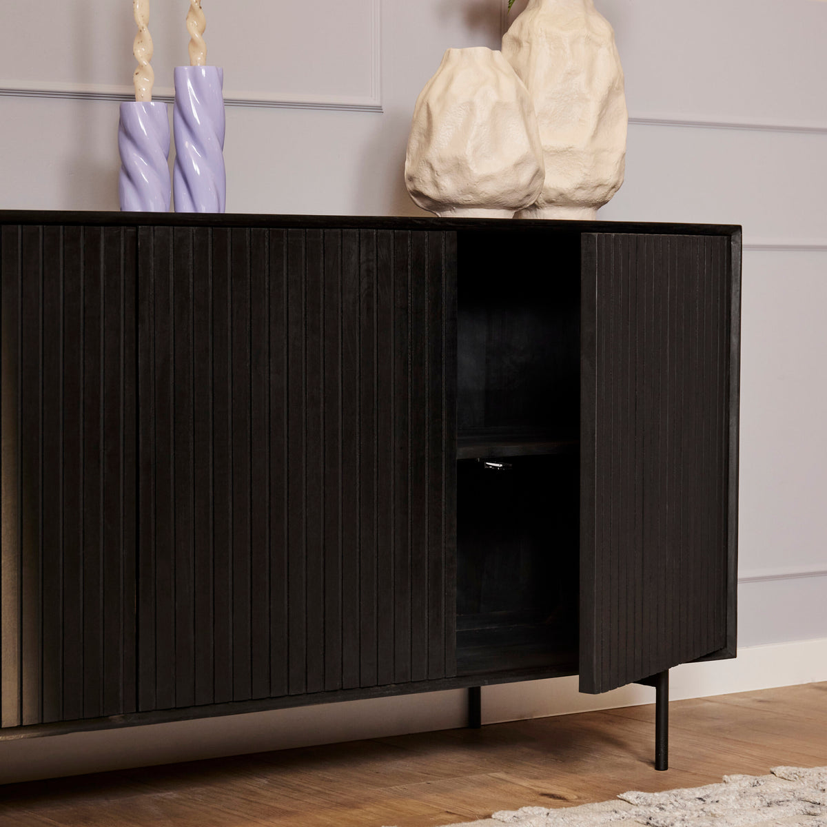 Zwart dressoir met open vakken en verticale ribbels, kastdeur deels open.