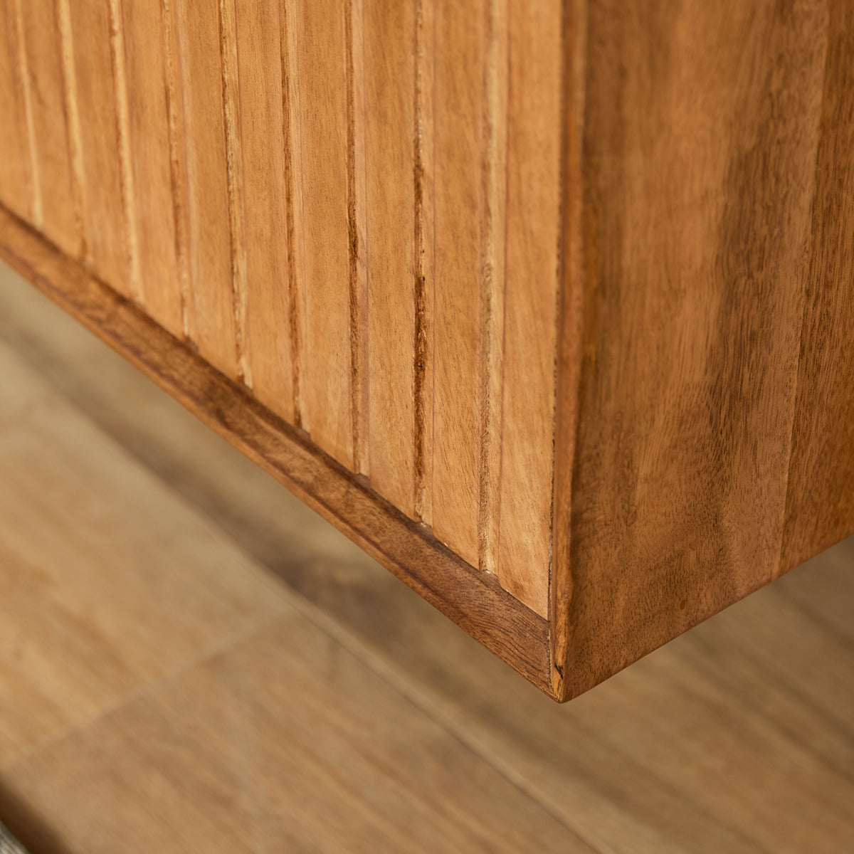 Hoek van naturel houten tv-meubel met verticale latten en strakke rand