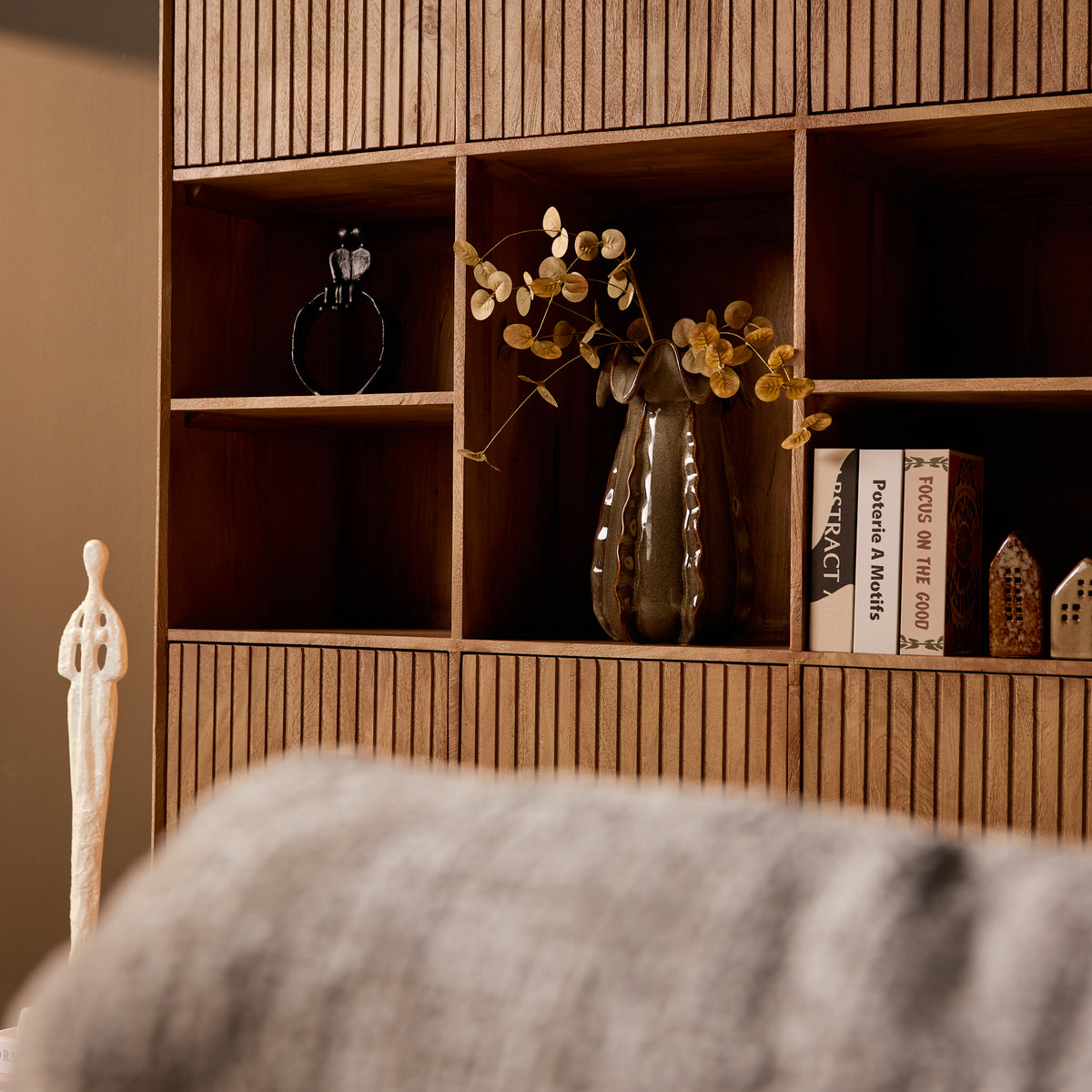 Open vakken in naturel houten vakkenkast met boeken en vaasdecor, deels zichtbaar.