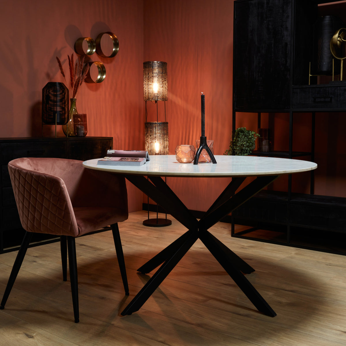 Ronde eetkamertafel met wit marmeren blad en zwart X-pootonderstel, met roze stoel.