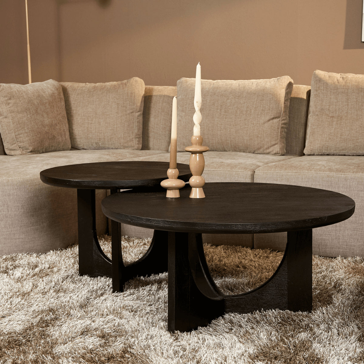Ronde zwarte salontafel met brede poten en houten blad, met decoratieve kaarsen erop