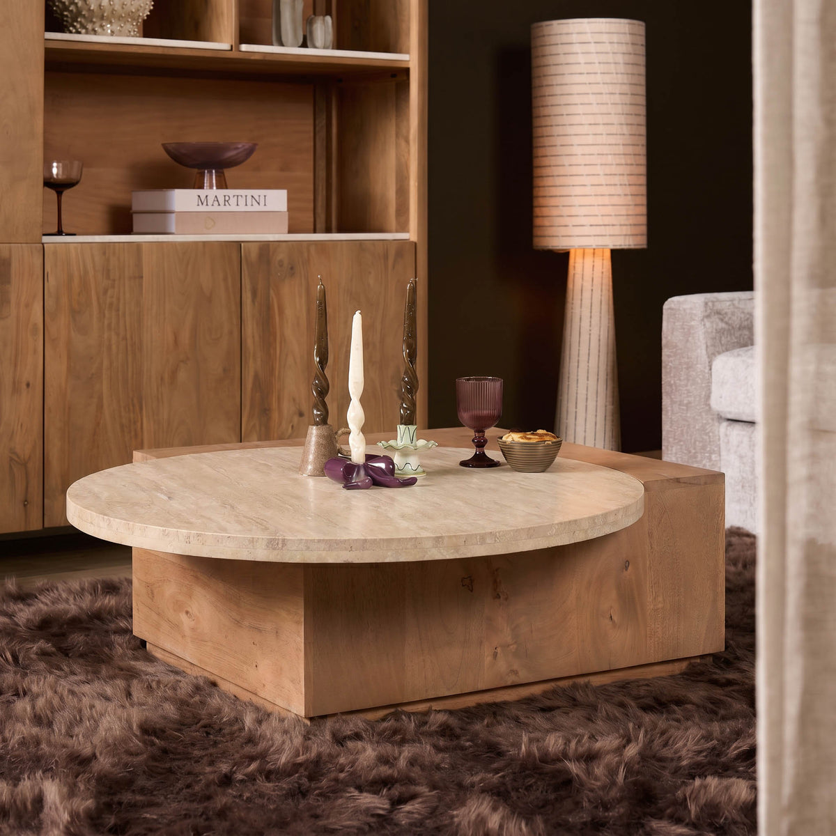Travertin salontafel met rond steenblad, houten onderstel en accessoires op het blad.