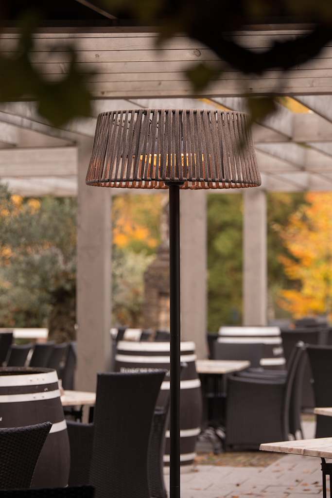 Terrasverwarmer op hoge zwarte paal met ronde, houtkleurige beschermkap.