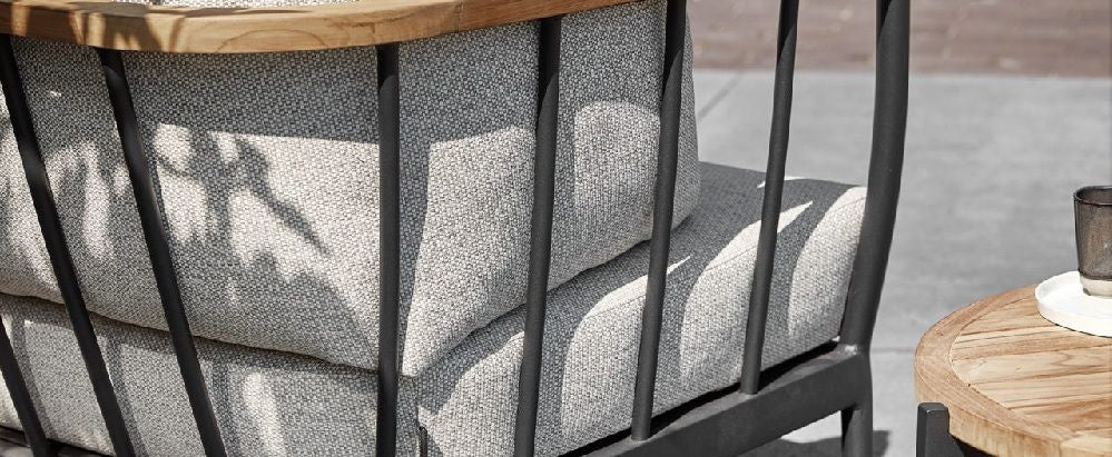 Loungebank zijkant met grijze stoffen bekleding, zwarte metalen buizen en armleuning