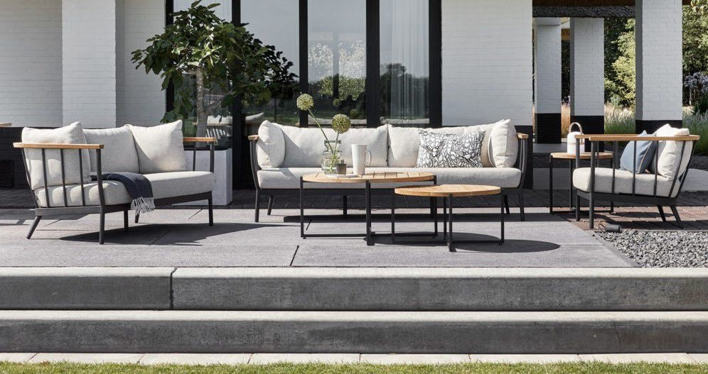 Loungebank op terras met lichte kussens, zwart frame en houten armleuningen
