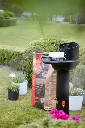 Zwarte houtskoolbarbecue op poot met deksel open en houtskoolcompartiment