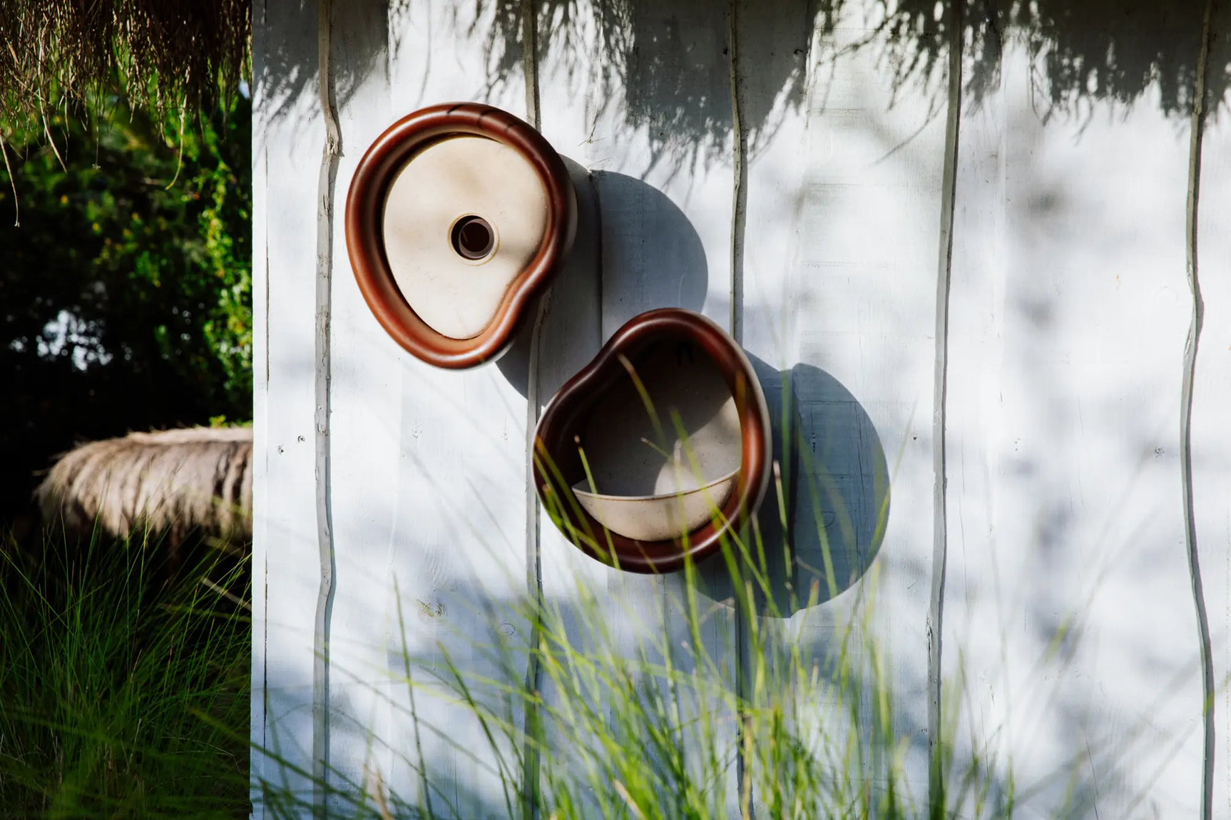 Twee vogelhuisjes, kastanje bruin en crèmekleurig, bevestigd op houten plank