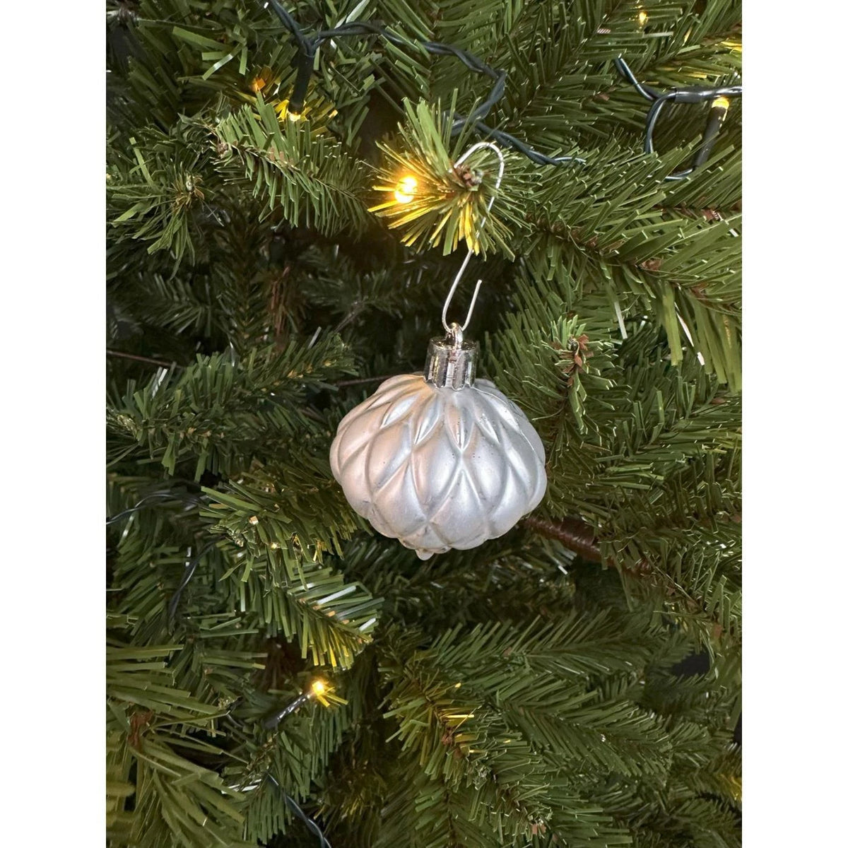 Zilveren kunststof kerstbal met ophanglus aan een kersttak