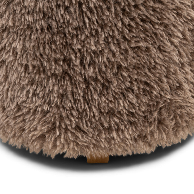 Detail van de pluizige bekleding en het houten voetje van de taupe poef