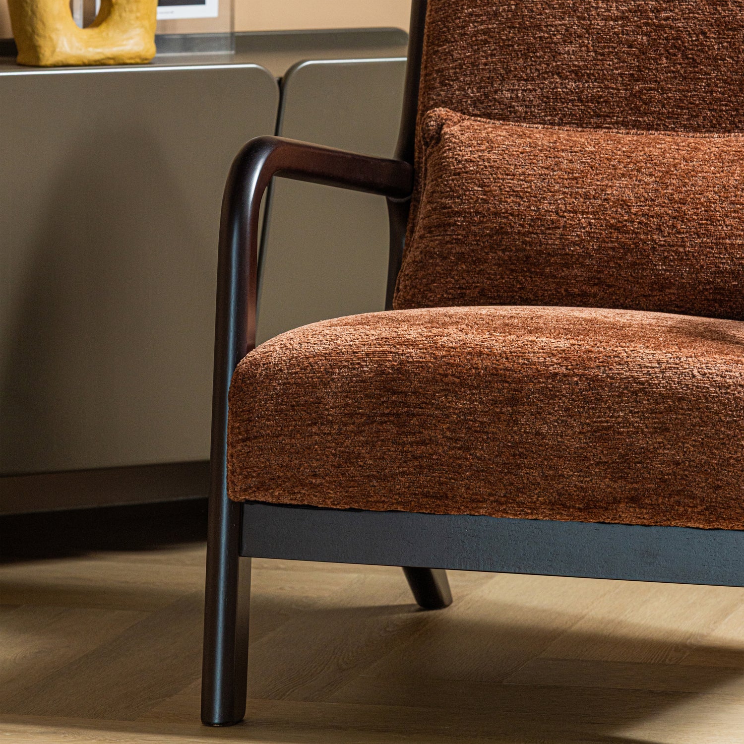 Bruine chenille fauteuil met donkere armleuning en afgeronde zijkant van de rug.