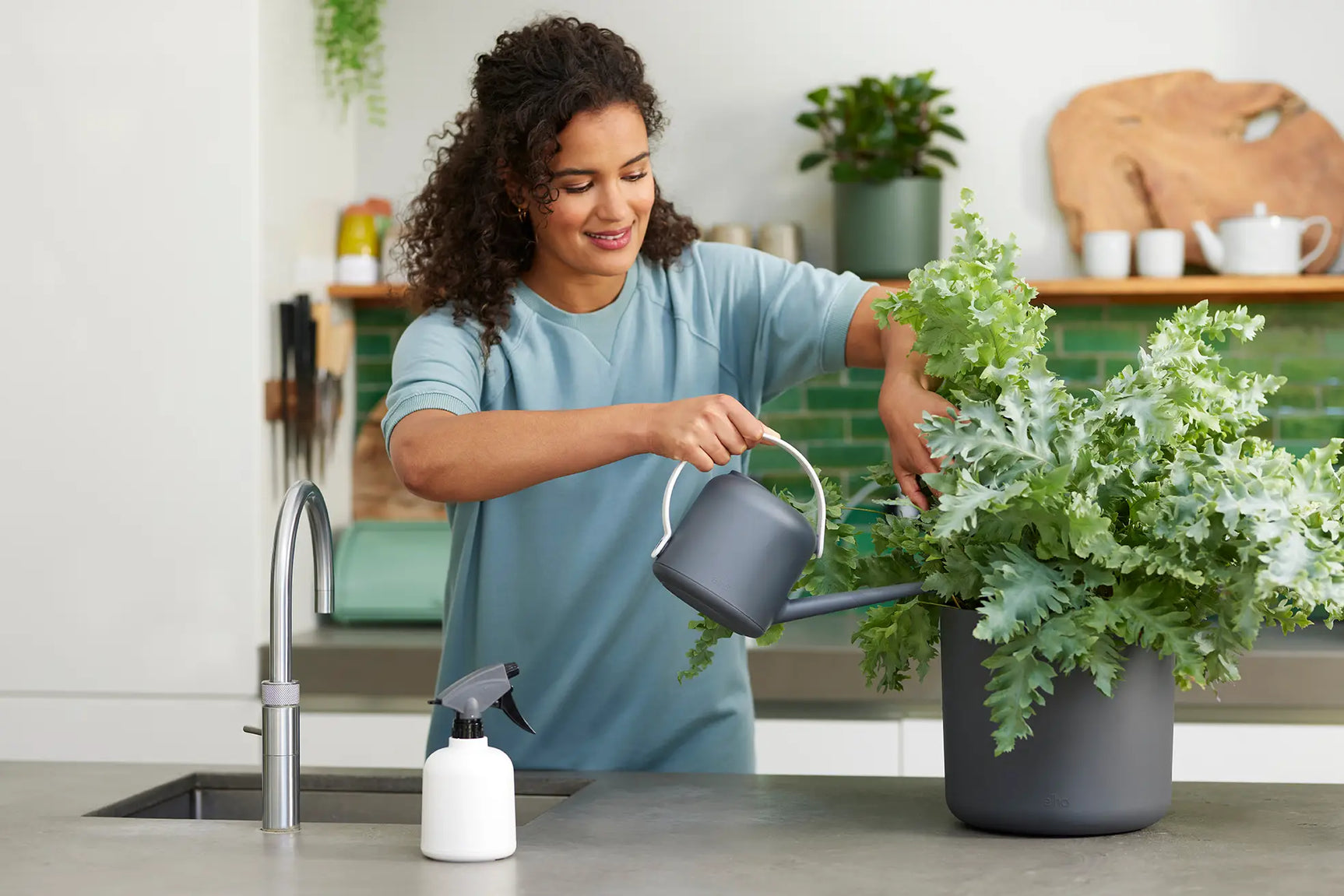 Grijze soft gieter die plantenwater geeft, vastgehouden boven een bloempot