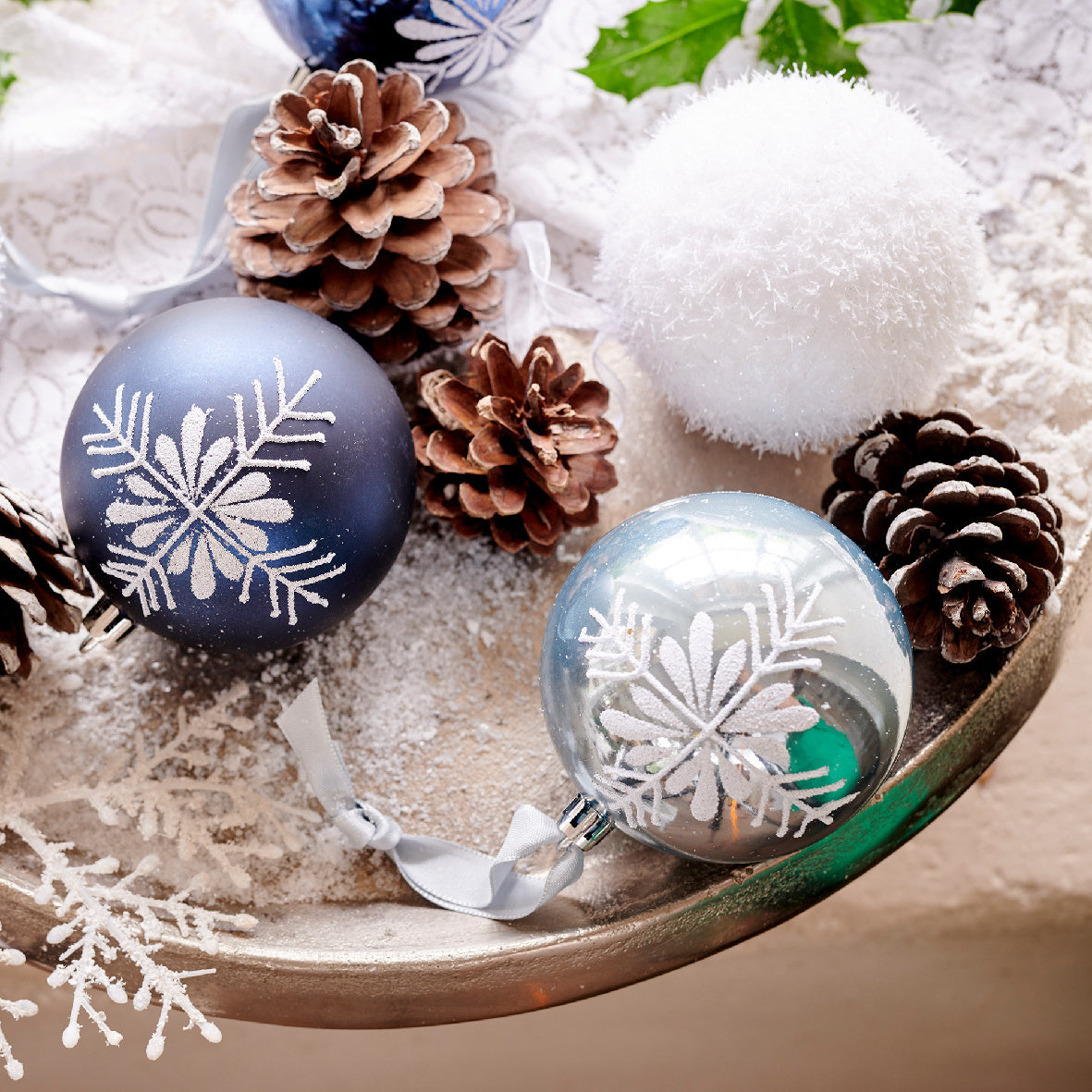 Schuim kerstbal met ijslaag op houten schaal, naast blauw en transparant kerstdecor