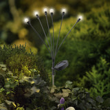 Zonne-energie priklamp met acht brandende lampjes op tuinbodem, met zonnepaneel