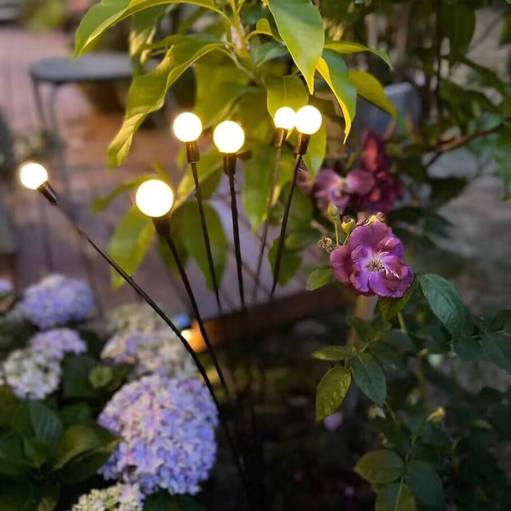 Zonne-energie priklamp met meerdere brandende lampjes tussen bladeren en bloemen
