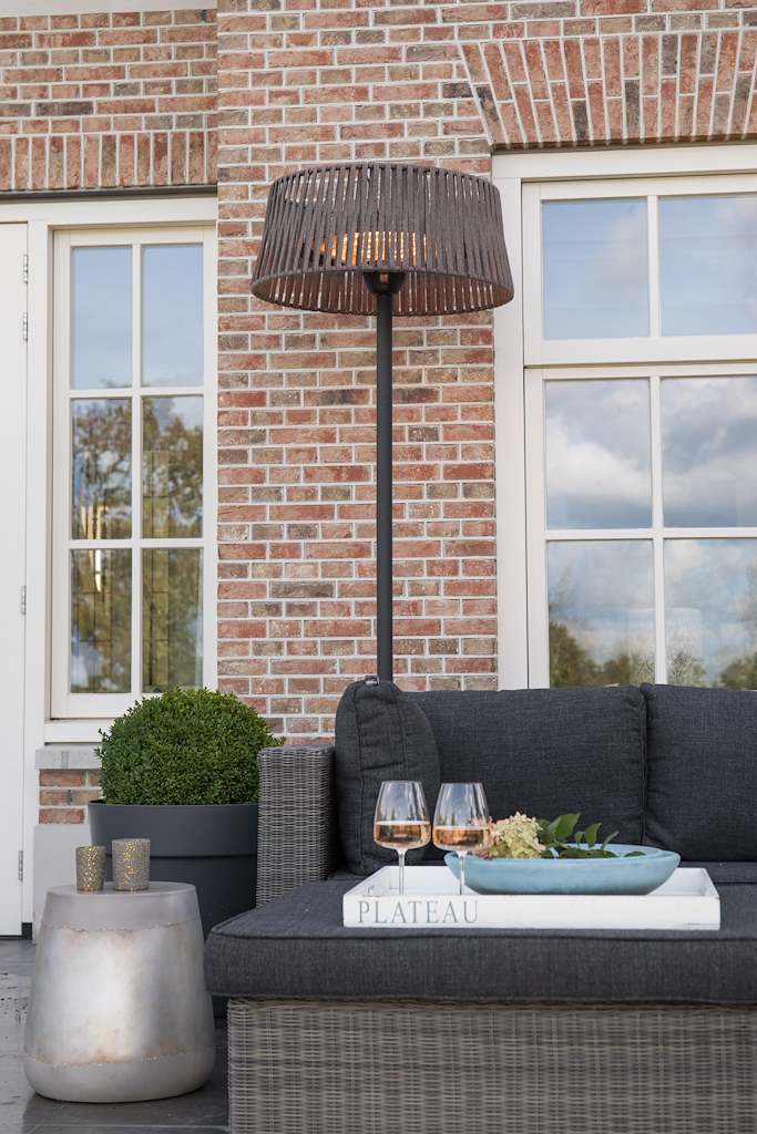 Staande terrasverwarmer met ronde kap naast buitentrampoline en donkergrijze bank.
