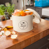 Keukencomposter in crème met open deksel en COMPOST-logo, gevuld met etensresten