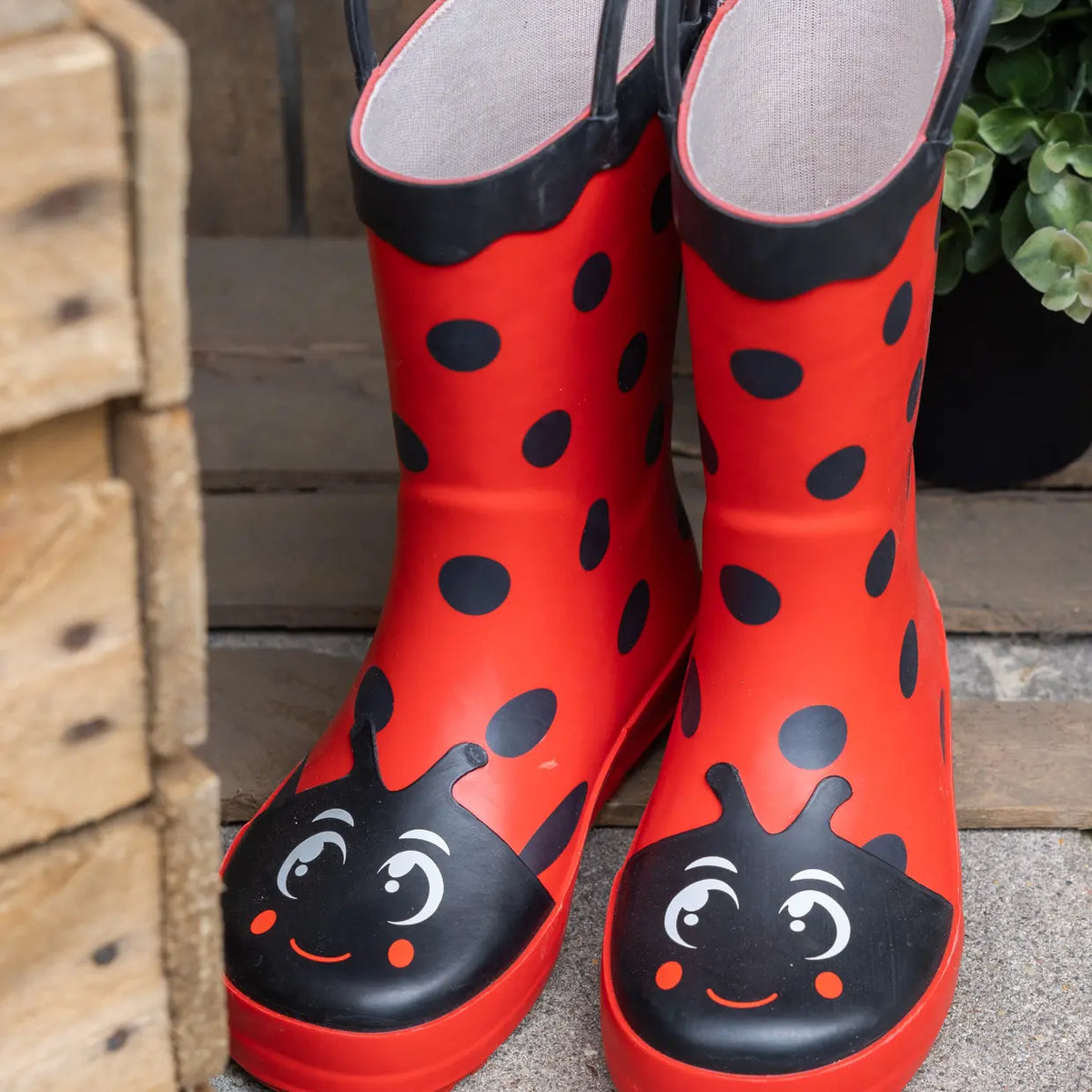Rode kinderlaarzen met lieveheersbeestprint, zwarte kraag en gezicht op de neus.