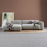 Lichtgrijze chaise longue bank met links chaise, sierkussen en bijzettafeltje.