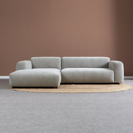 Lichtgrijze chaise longue bank met links chaise, twee rugkussens en lange zitting.