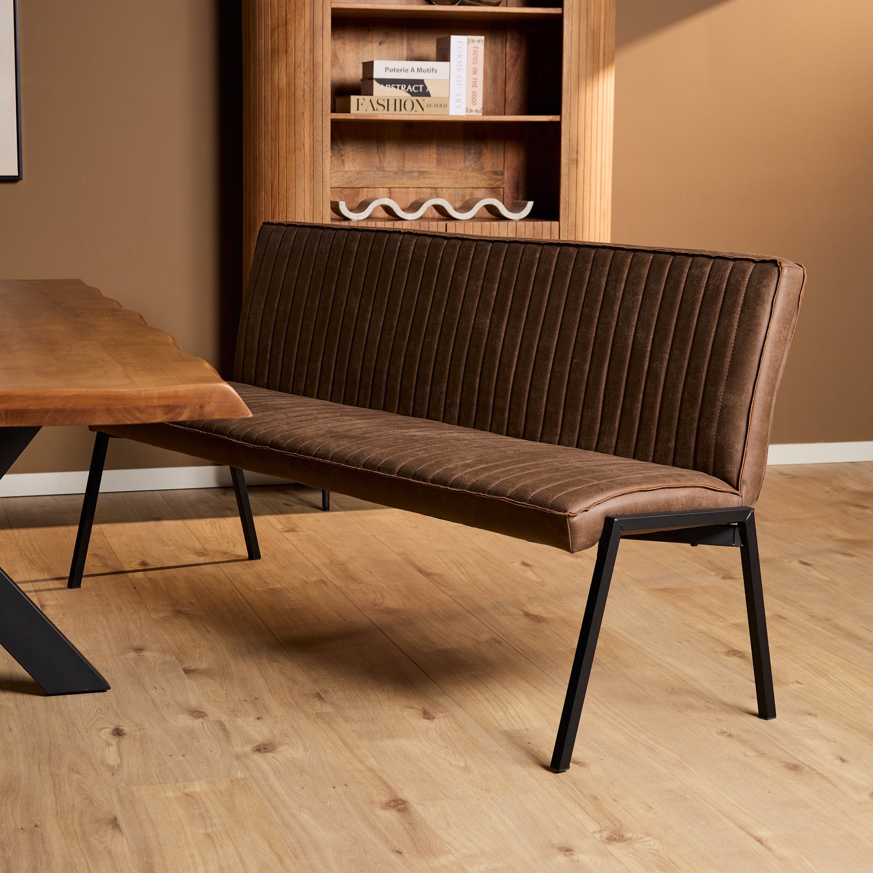 Bruine eetkamerbank met ribbelstoffering, brede zitting en rugleuning, zwarte metalen poten.