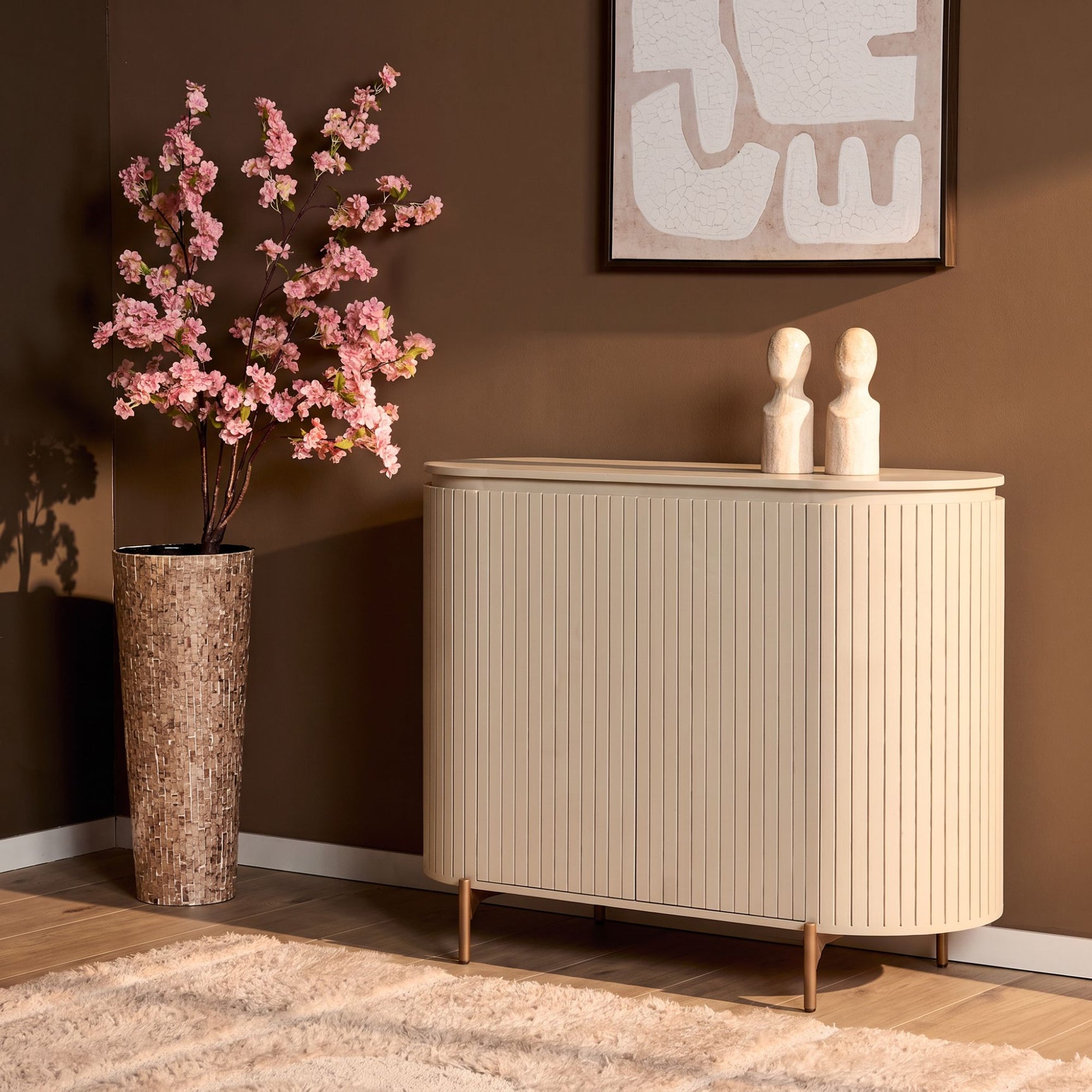 Zandkleurig dressoir met verticale ribbels, ronde bovenkant en houten poten.
