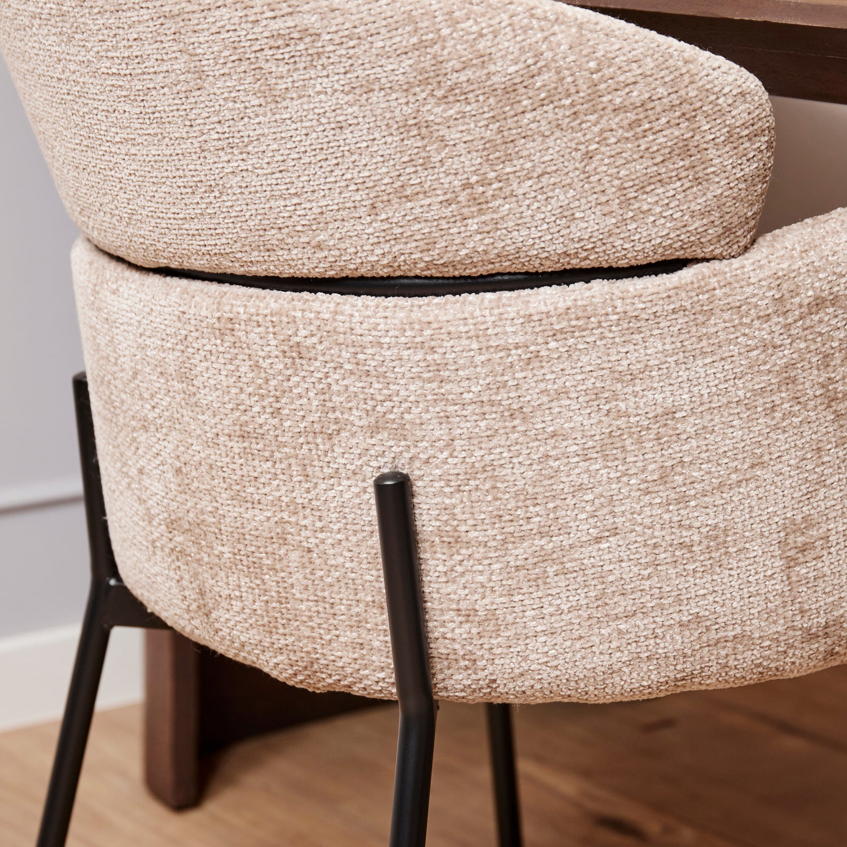 Detail van beige gestoffeerde eetkamerstoel met armleuning, zwarte poot en afgeronde rug