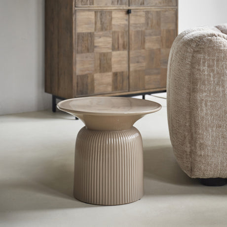 Zandkleurige Cascais bijzettafel met rond blad en geribbelde voet naast een fauteuil