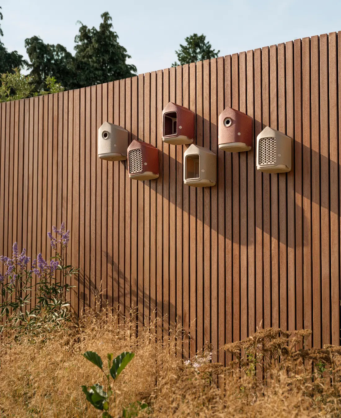 Meerdere rode vogelhuisjes met rond invlieggat, bevestigd op een verticale plank.