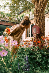 Rood insectenhotel aan een boomstronk in een tuin met bloemen