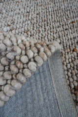 Beige vloerkleeddetail met ronde wolknoppen en lichtgekleurde rand