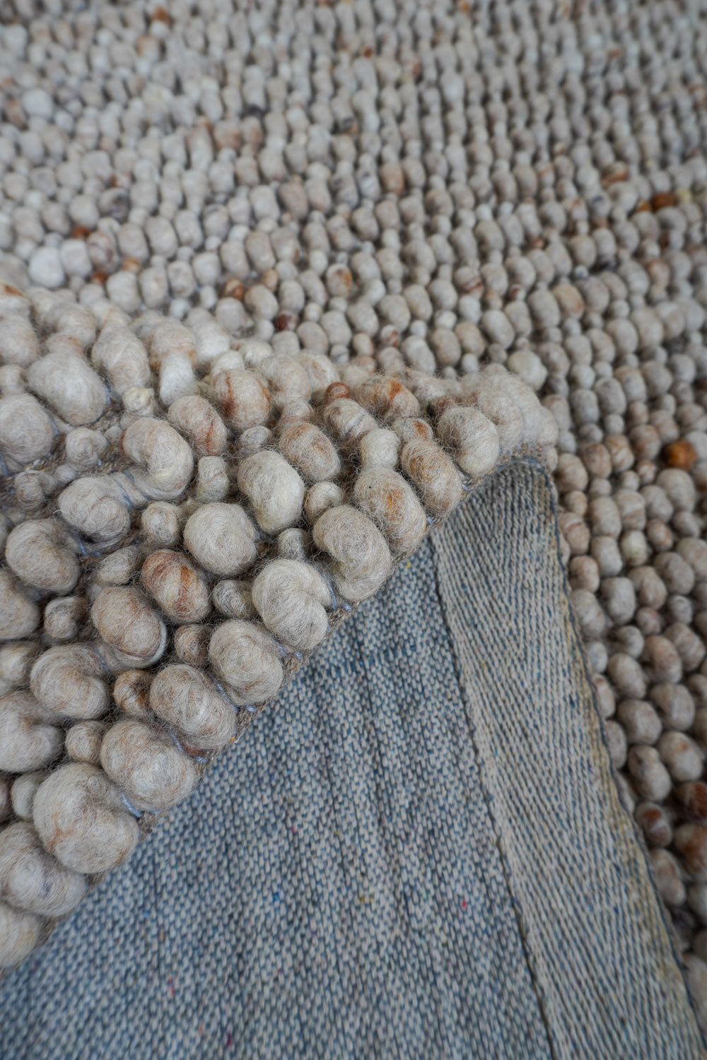 Beige vloerkleeddetail met ronde wolknoppen en lichtgekleurde rand