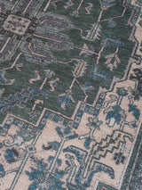 Vloerkleed close-up met geometrisch patroon in donkergroen, beige en blauw met ornamentranden