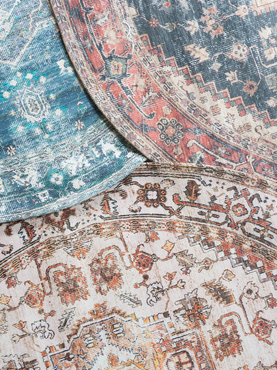 Rond vloerkleed detail: lichtgrijze basis met bruin, blauw en rood ornamenten en rand