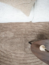 Taupe vloerkleed met ingedrukt, golvend reliëf en geribde banen; close-up